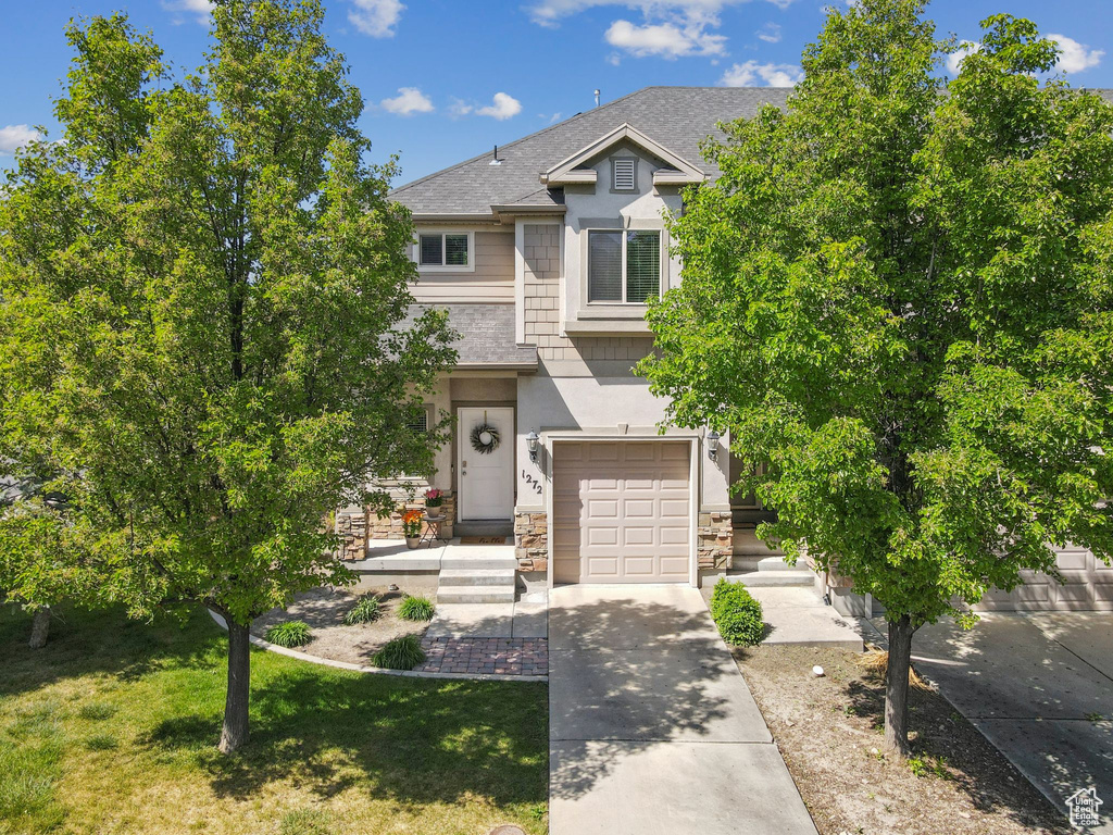 View of front of property featuring an attached garage, concrete driveway, a shingled roof, stone siding, and a front lawn