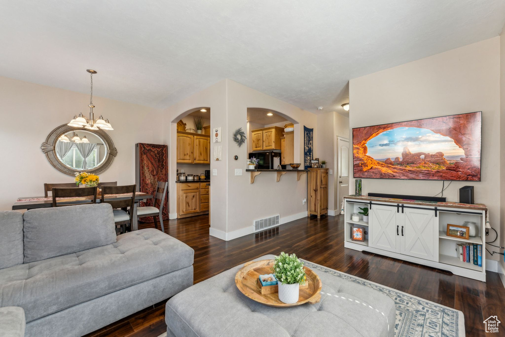 Living area featuring a chandelier, arched walkways, dark wood-style flooring, and baseboards