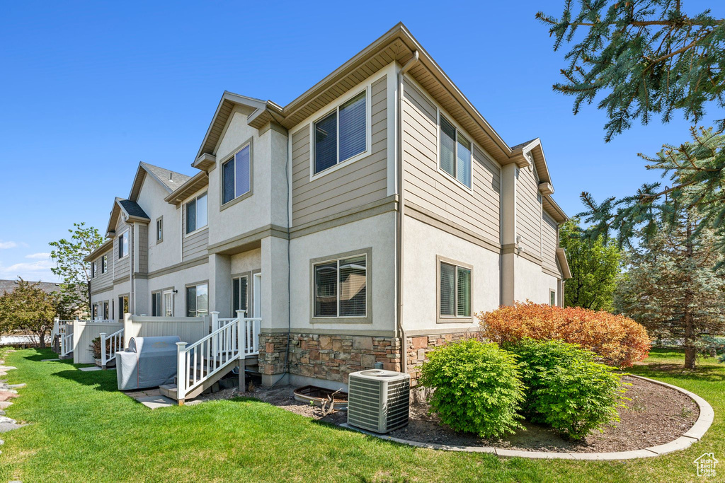 Back of property featuring central AC, stone siding, a yard, and stucco siding