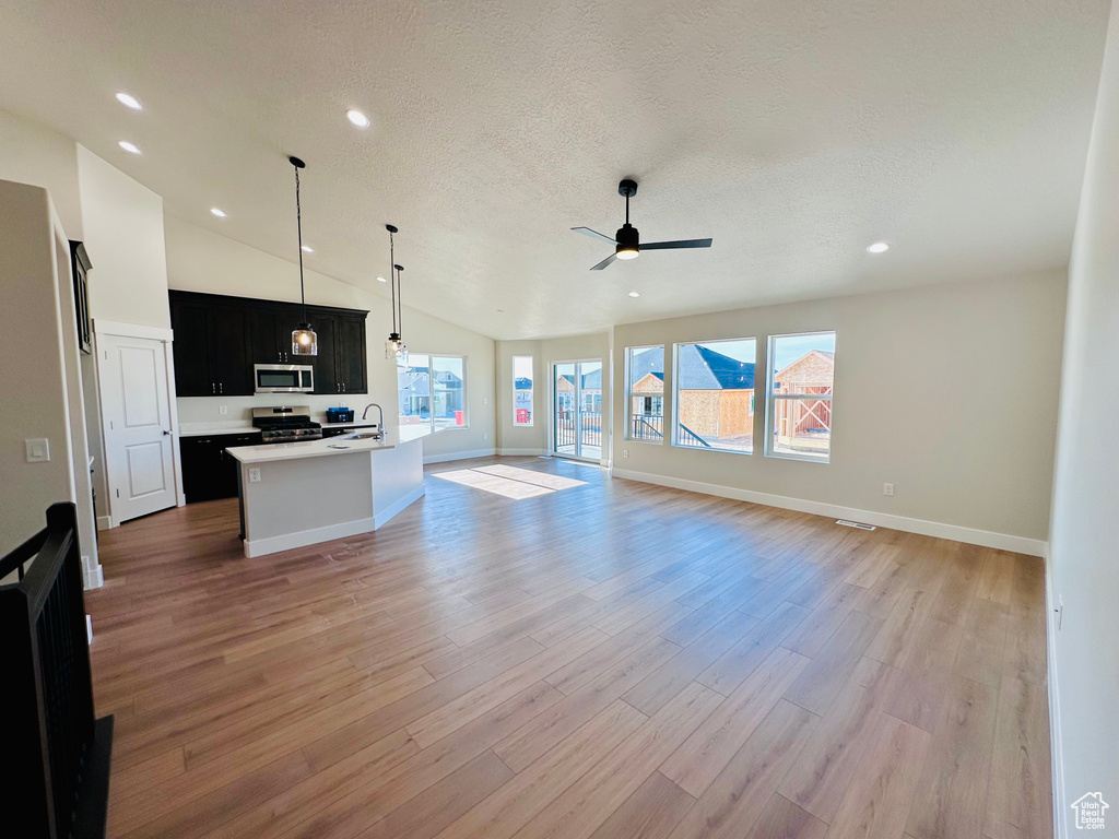 Unfurnished living room with a sink, a ceiling fan, lofted ceiling, light wood-type flooring, and baseboards