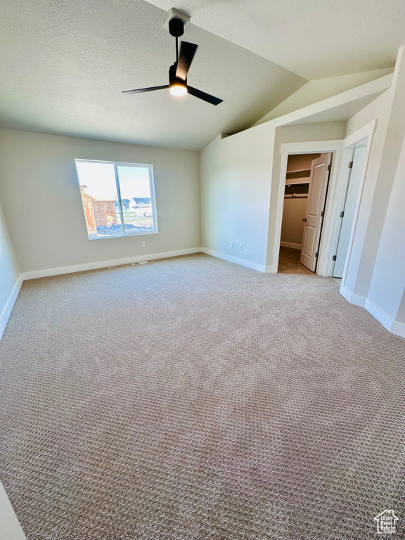 Unfurnished bedroom featuring light colored carpet, baseboards, vaulted ceiling, a walk in closet, and a ceiling fan