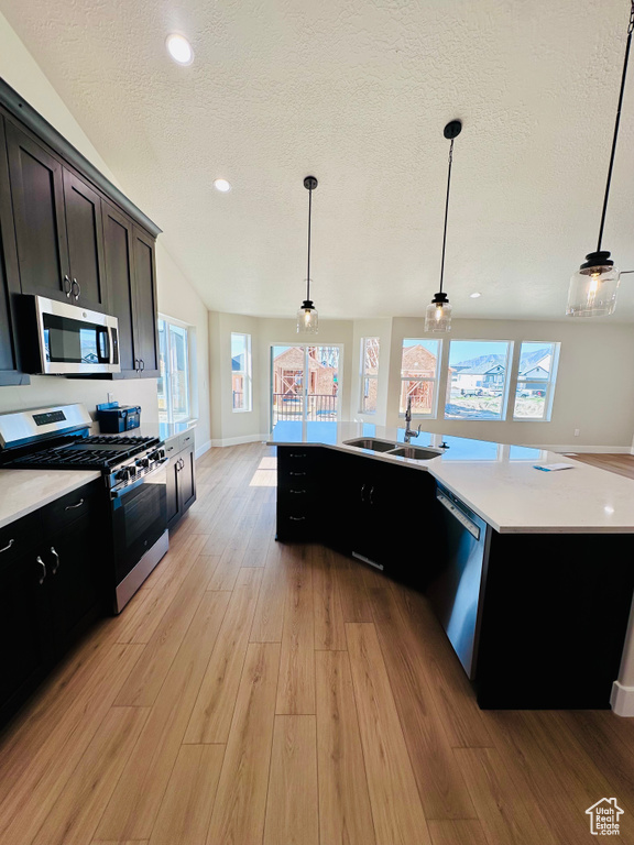 Kitchen featuring appliances with stainless steel finishes, a sink, light wood finished floors, a textured ceiling, and light countertops