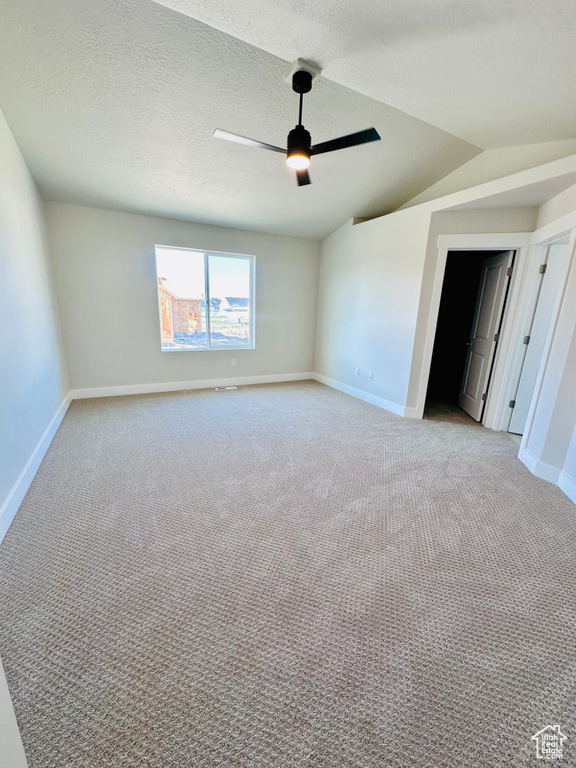 Empty room featuring light colored carpet, a ceiling fan, baseboards, lofted ceiling, and a textured ceiling