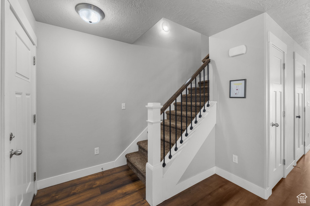 Stairs with baseboards, wood finished floors, and a textured ceiling