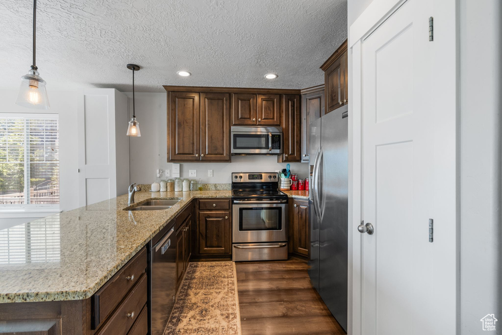 Kitchen featuring appliances with stainless steel finishes, a sink, a peninsula, dark wood-style floors, and a textured ceiling