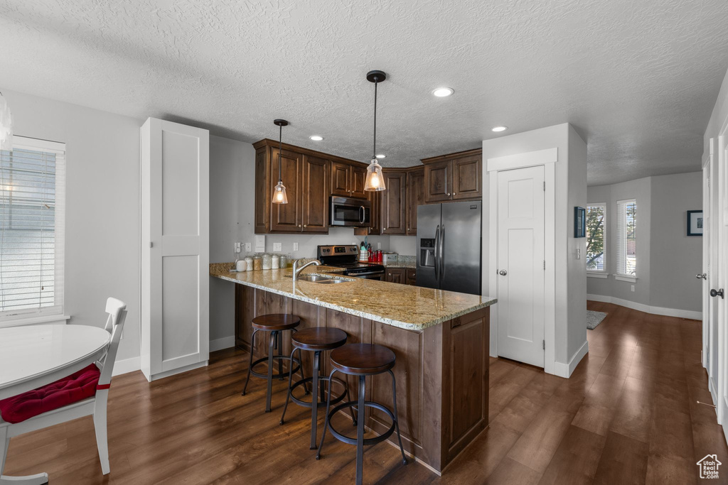 Kitchen with appliances with stainless steel finishes, baseboards, a sink, a peninsula, and a textured ceiling