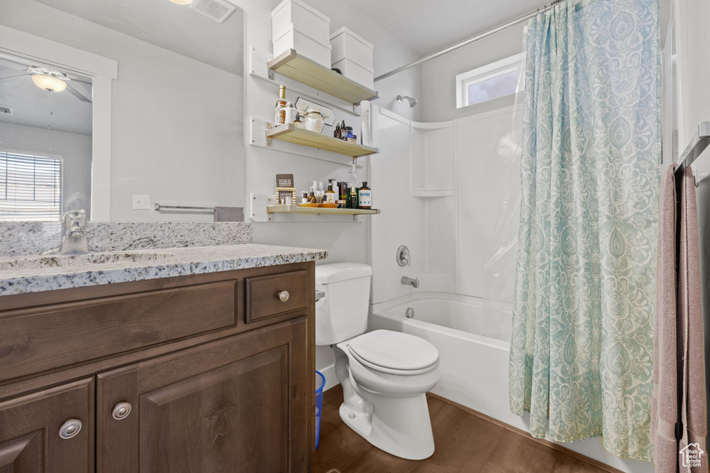 Bathroom with wood finished floors, shower / bath combo with shower curtain, vanity, toilet, and ceiling fan