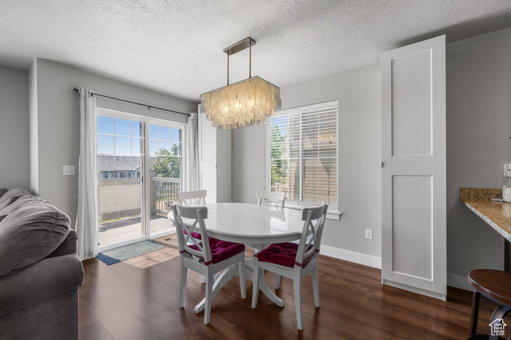 Dining area featuring a chandelier, dark wood finished floors, healthy amount of natural light, a textured ceiling, and baseboards