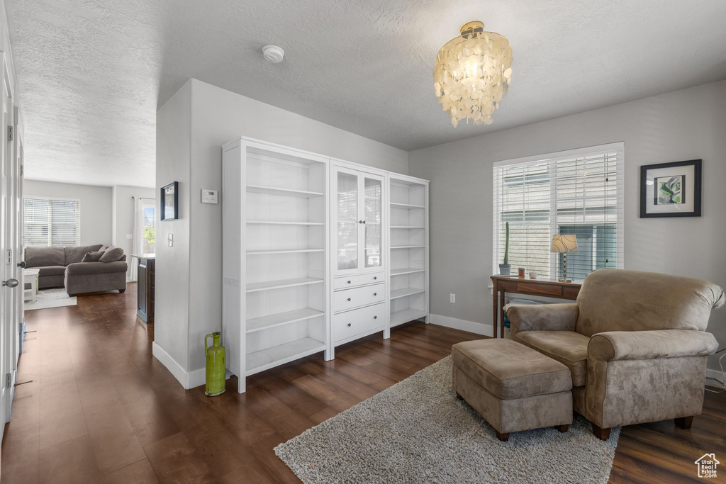 Sitting room with baseboards, dark wood finished floors, a chandelier, and a textured ceiling