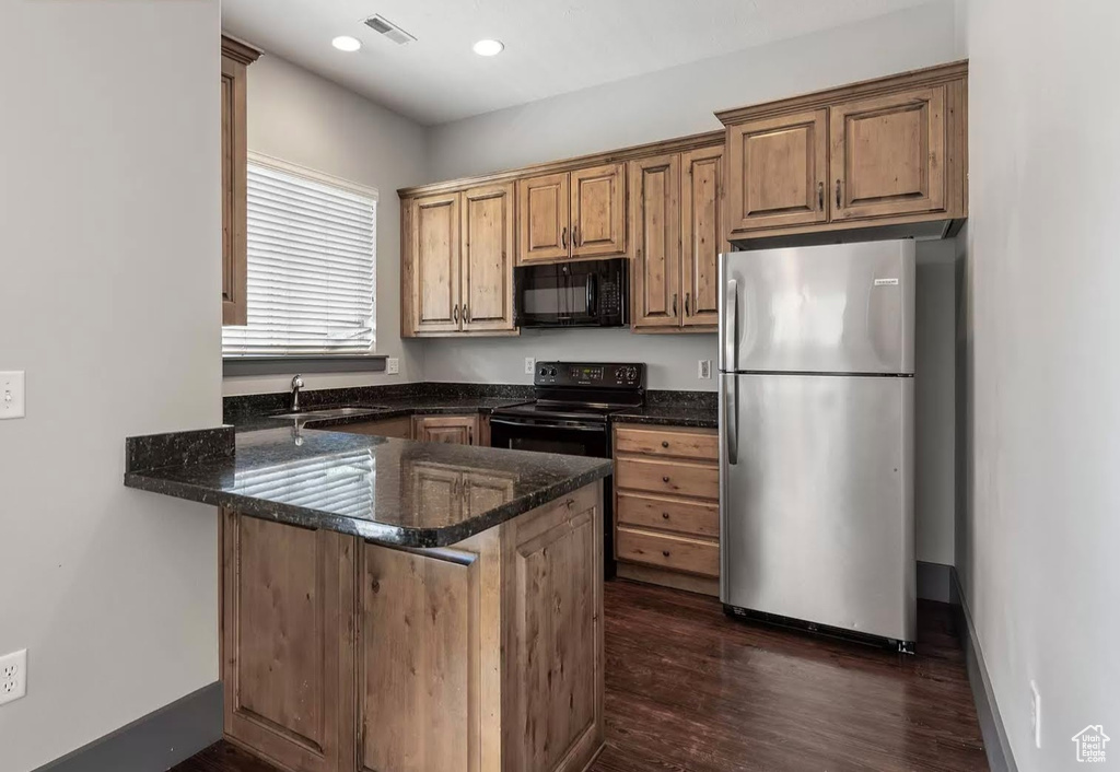 Kitchen with black appliances, a peninsula, a sink, dark stone countertops, and dark wood-style flooring