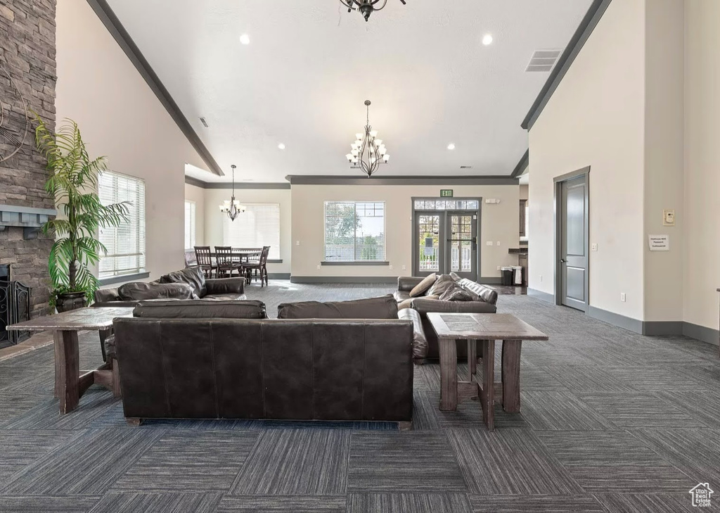 Living area with dark colored carpet, a chandelier, high vaulted ceiling, ornamental molding, and baseboards