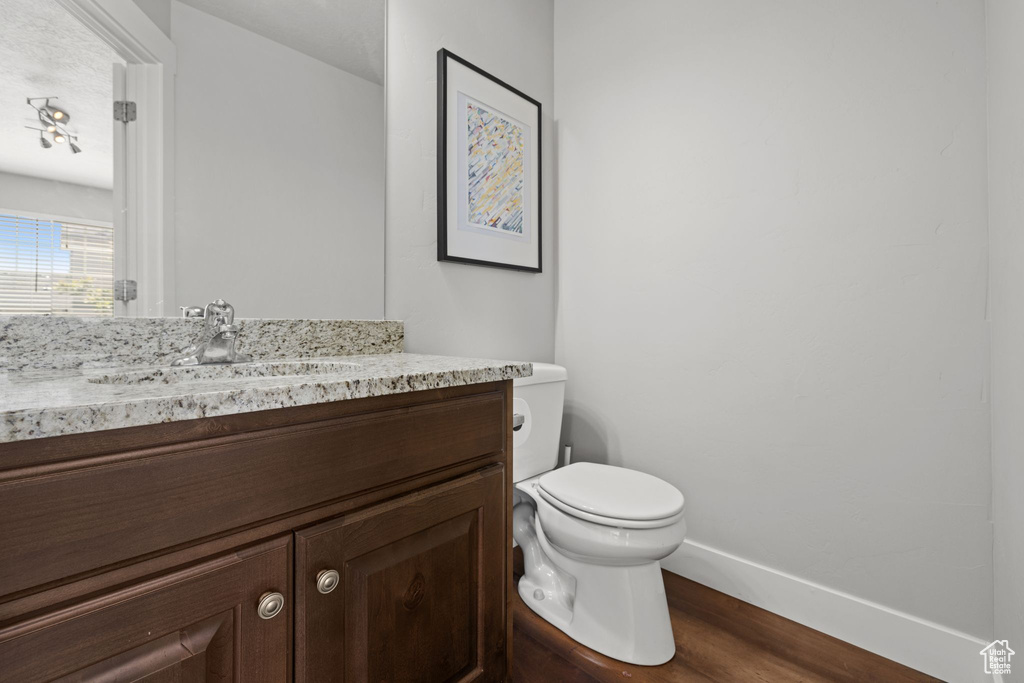 Bathroom featuring vanity, toilet, wood finished floors, and baseboards