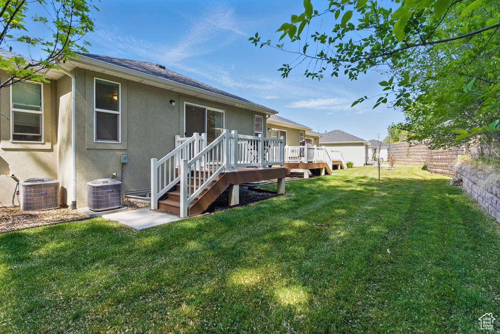 Rear view of property featuring stucco siding, a wooden deck, central AC unit, and roof with shingles