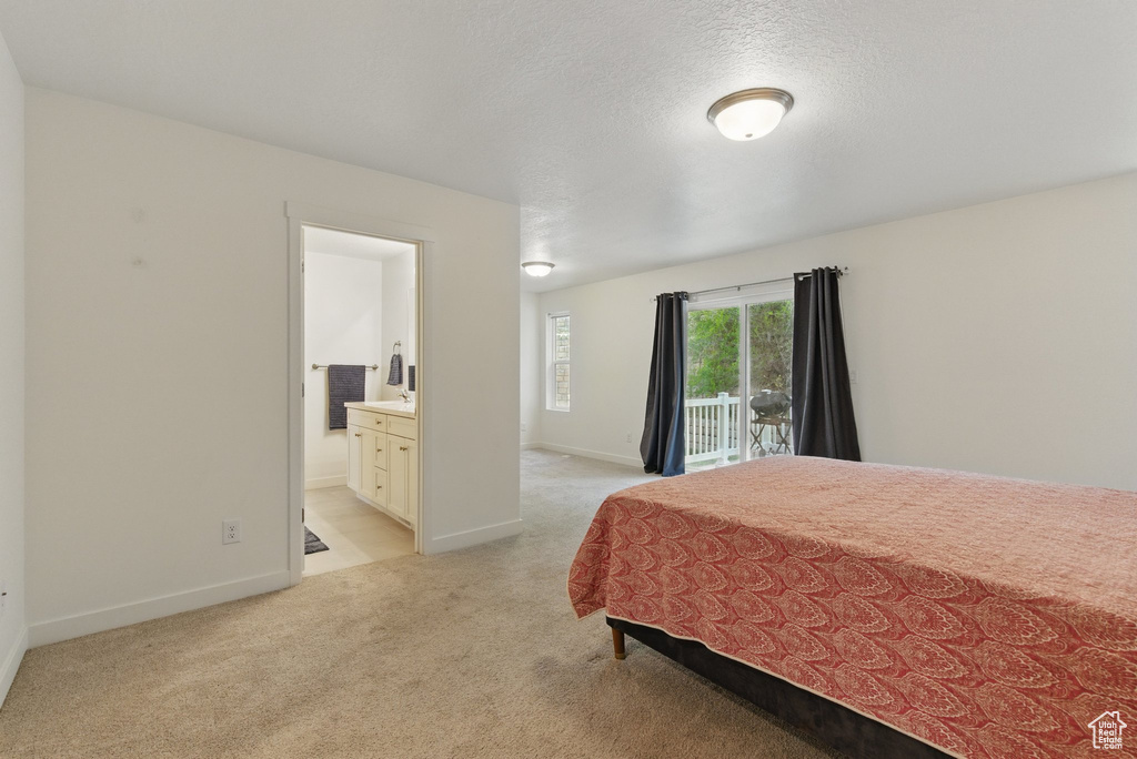 Bedroom with light carpet, access to exterior, ensuite bath, and baseboards