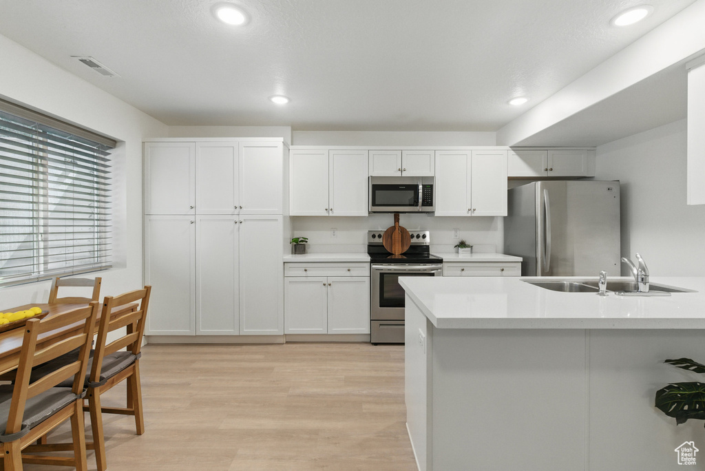 Kitchen featuring stainless steel appliances, a sink, light countertops, recessed lighting, and white cabinets