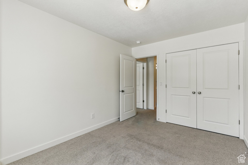 Unfurnished bedroom with carpet, baseboards, a closet, and a textured ceiling