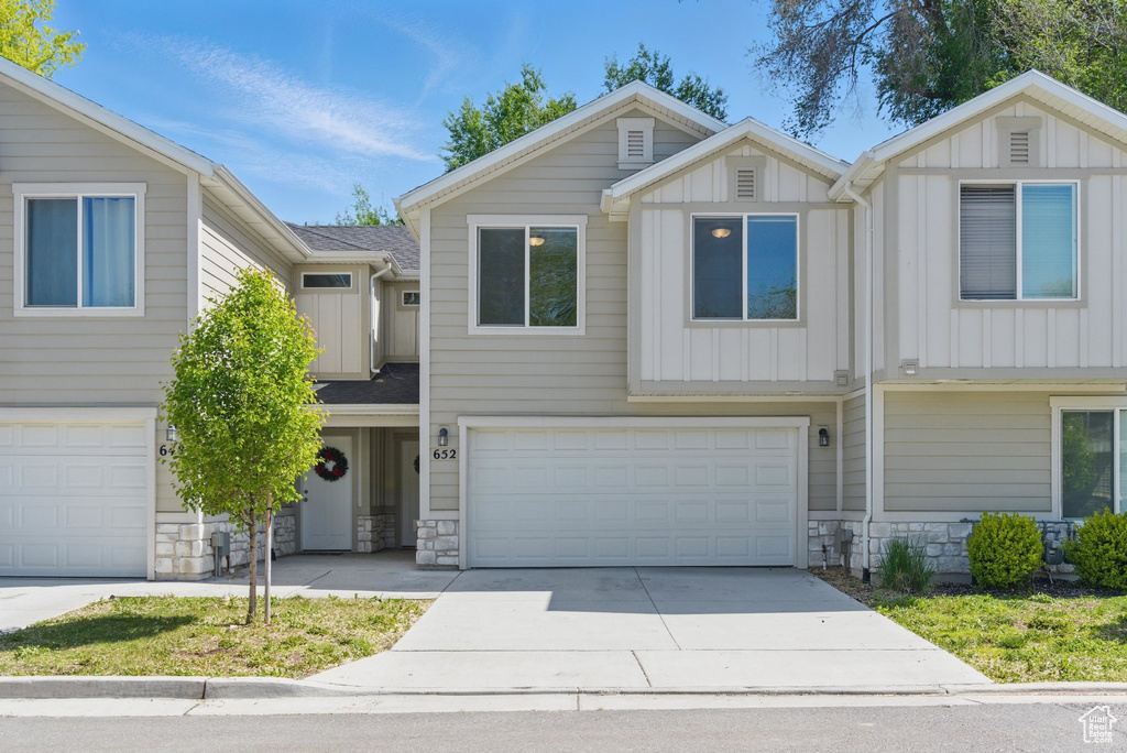 Townhome / multi-family property featuring board and batten siding, stone siding, concrete driveway, and an attached garage