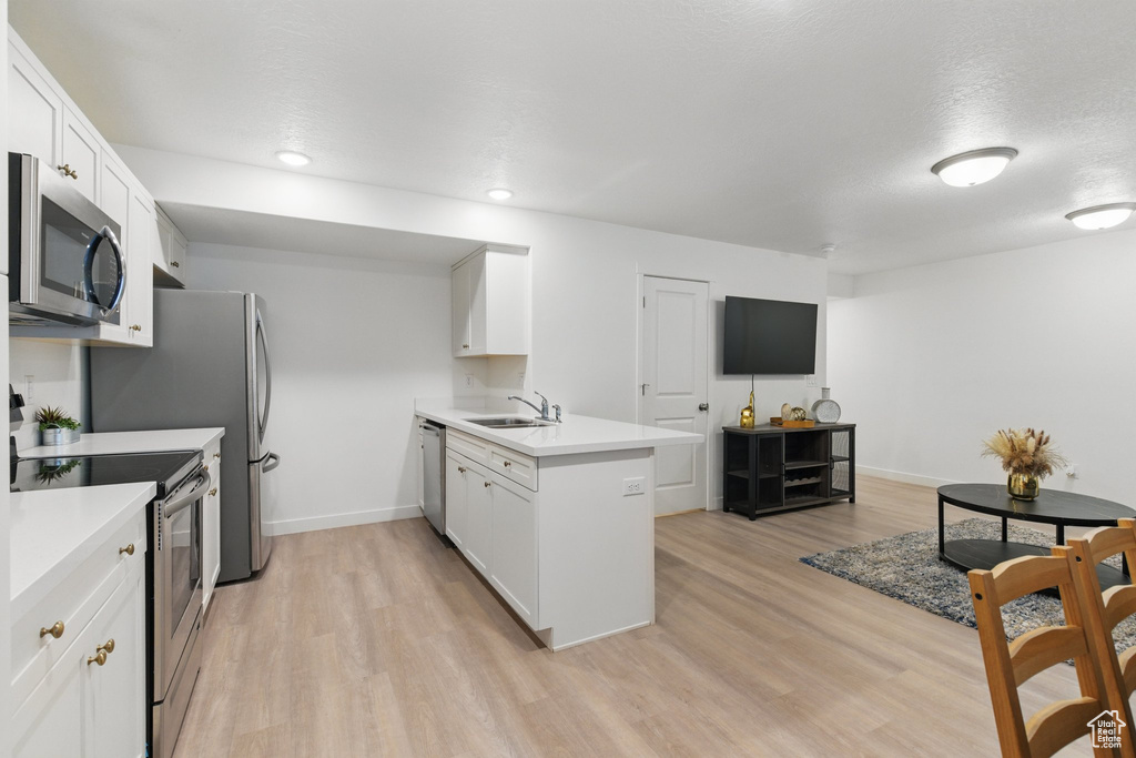 Kitchen featuring appliances with stainless steel finishes, a sink, a peninsula, white cabinets, and recessed lighting
