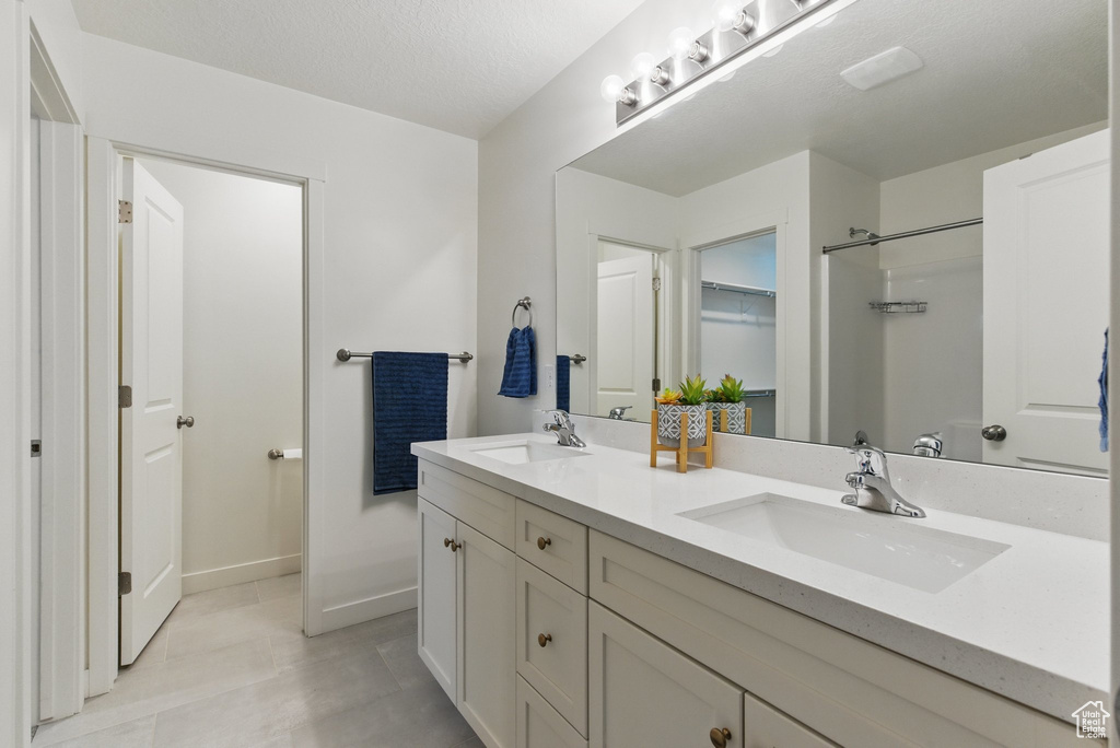 Bathroom with double vanity, baseboards, tile patterned floors, and a shower