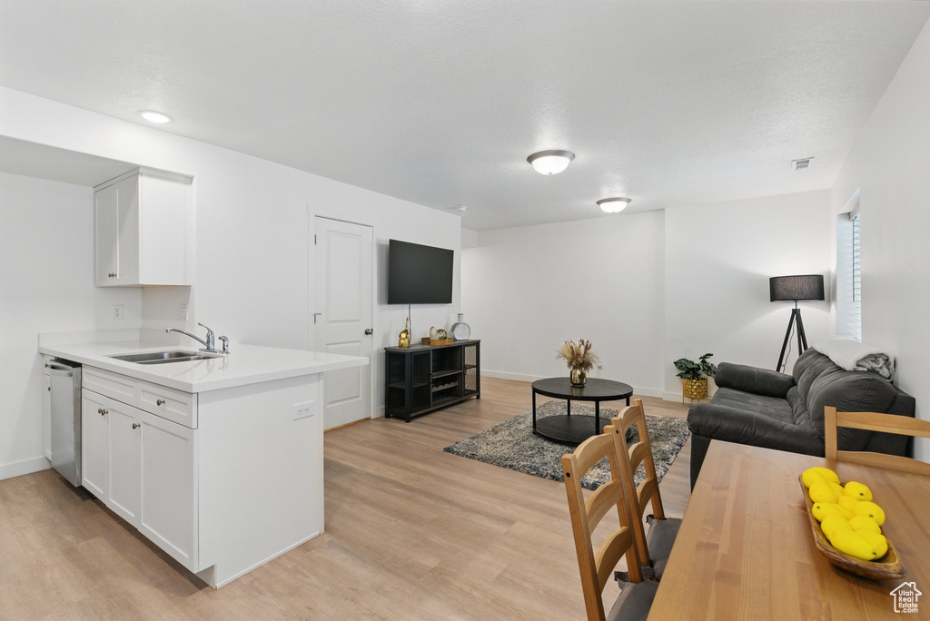 Kitchen with a sink, stainless steel dishwasher, open floor plan, light countertops, and light wood-style flooring