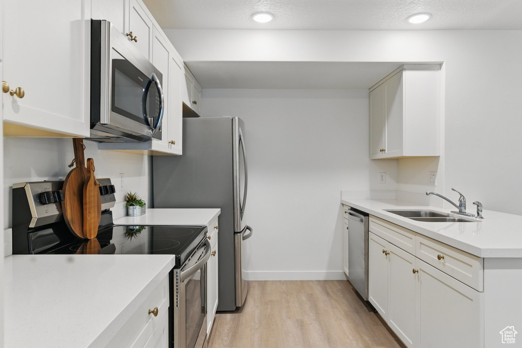 Kitchen featuring appliances with stainless steel finishes, a sink, light wood finished floors, light countertops, and white cabinets