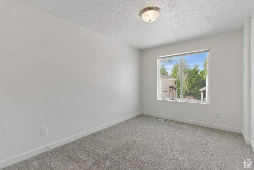 Unfurnished room featuring a textured ceiling, light carpet, and baseboards