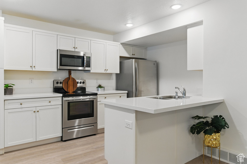 Kitchen with stainless steel appliances, a sink, a peninsula, recessed lighting, and light wood-type flooring