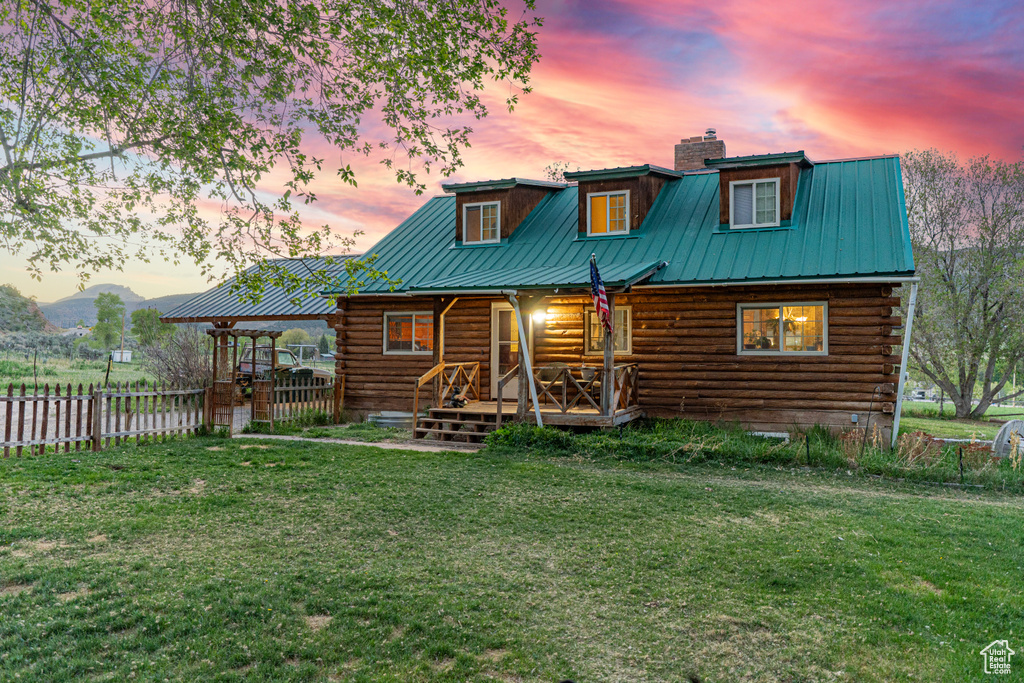 Back of house at dusk with log exterior, a chimney, metal roof, and covered porch