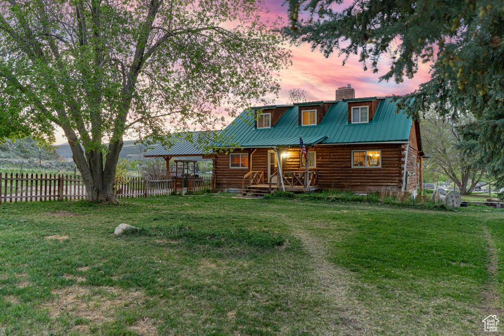 Back of house at dusk with log siding, covered porch, a chimney, and metal roof