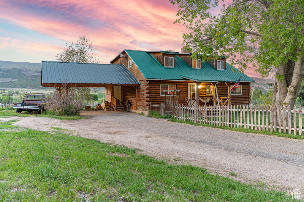 Log-style house with log siding, dirt driveway, metal roof, a porch, and a fenced front yard