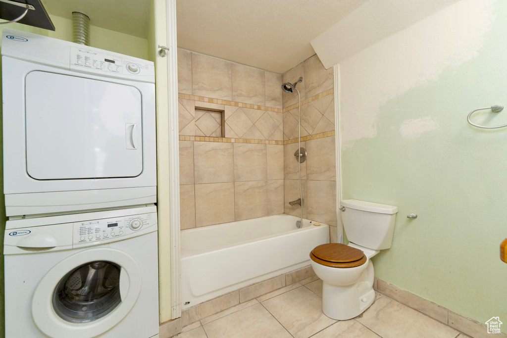 Full bath with stacked washer and clothes dryer, tile patterned flooring, baseboards, toilet, and bathing tub / shower combination