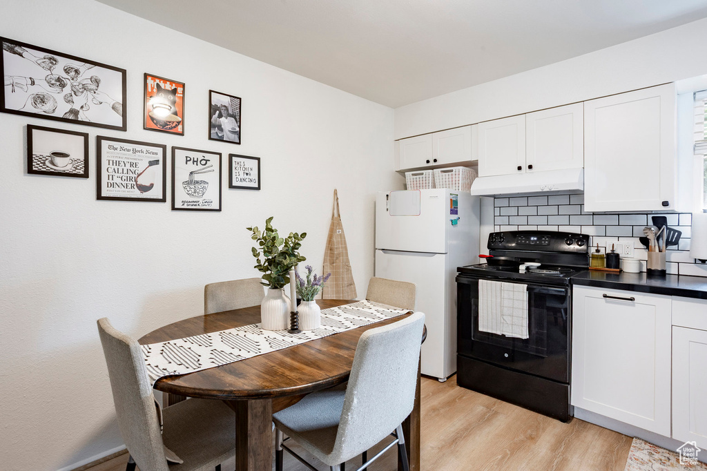 Kitchen with electric range, under cabinet range hood, freestanding refrigerator, backsplash, and light wood-type flooring