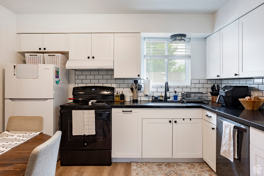 Kitchen with black electric range oven, freestanding refrigerator, under cabinet range hood, a sink, and dishwasher