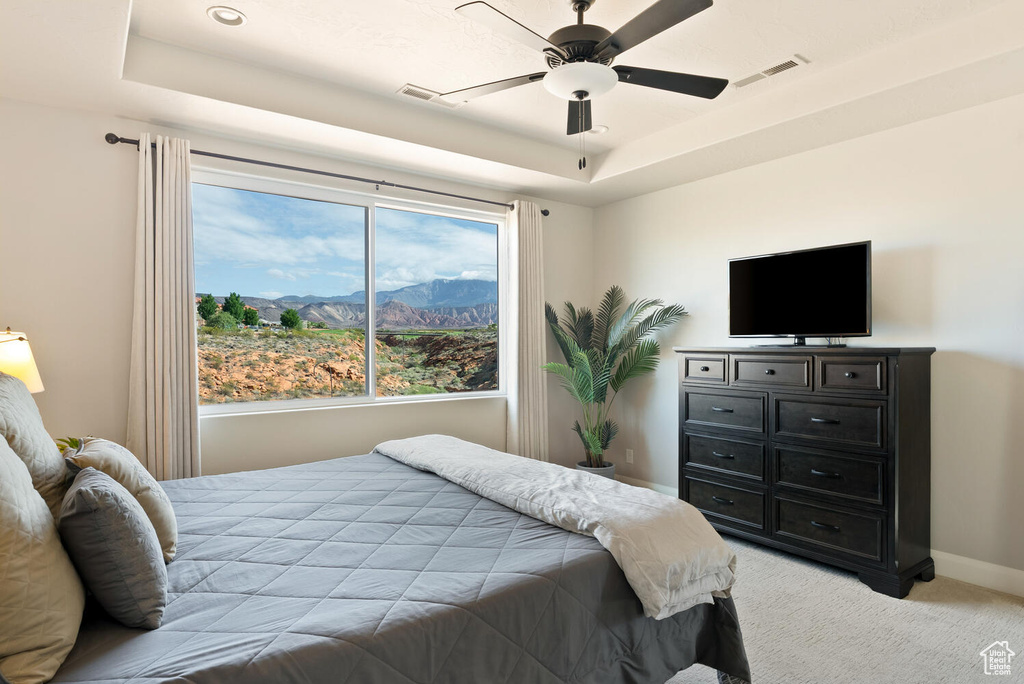 Bedroom featuring a tray ceiling, light carpet, baseboards, and ceiling fan