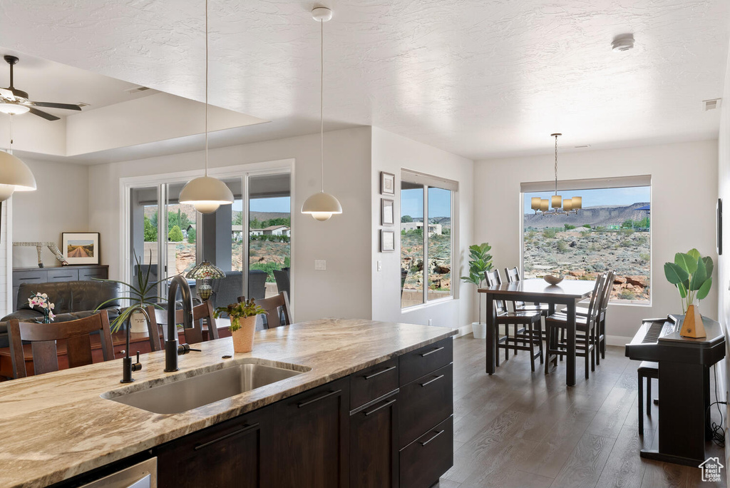 Kitchen with a sink, dark wood-style flooring, light stone counters, a chandelier, and pendant lighting