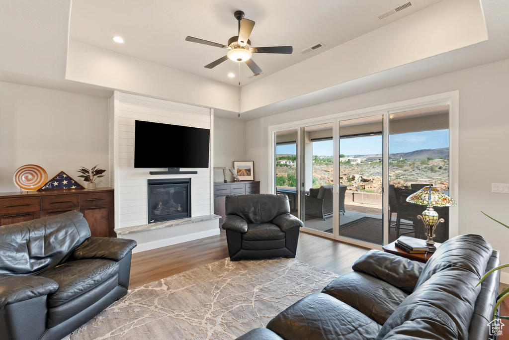 Living area featuring a ceiling fan, wood finished floors, a large fireplace, recessed lighting, and a tray ceiling
