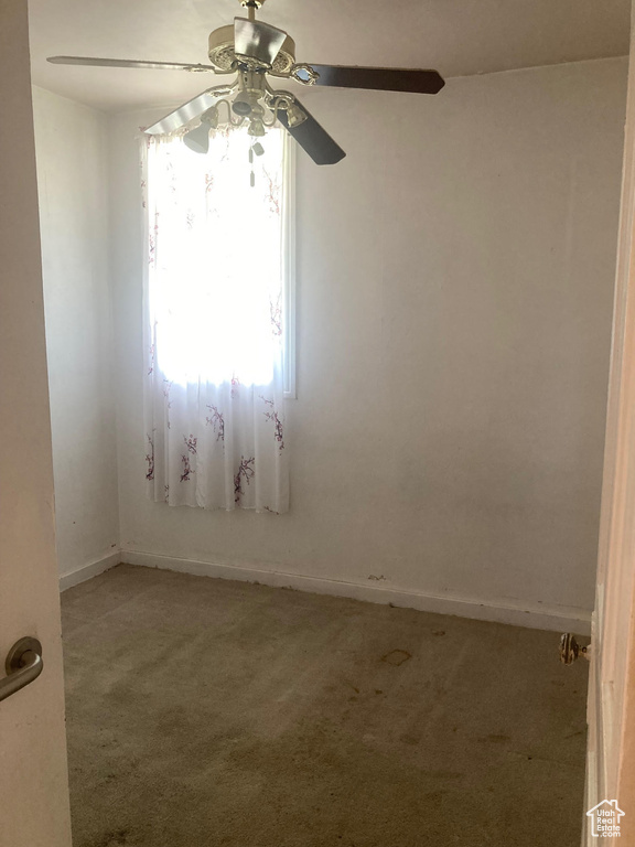 Empty room featuring light carpet, a ceiling fan, and baseboards