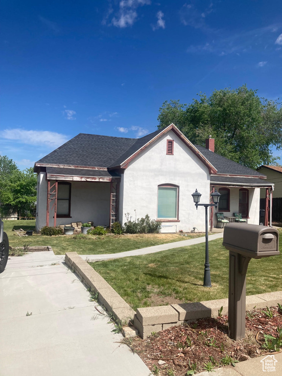 Ranch-style house with a front yard, a shingled roof, a chimney, a porch, and stucco siding