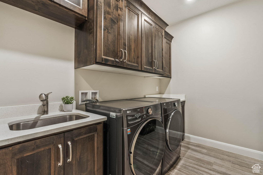 Clothes washing area featuring cabinet space, washing machine and dryer, baseboards, and light wood-style floors