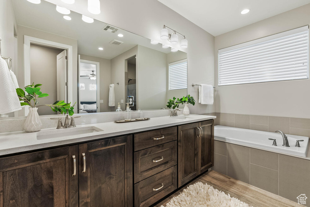 Bathroom featuring wood finished floors, double vanity, a garden tub, and ensuite bathroom