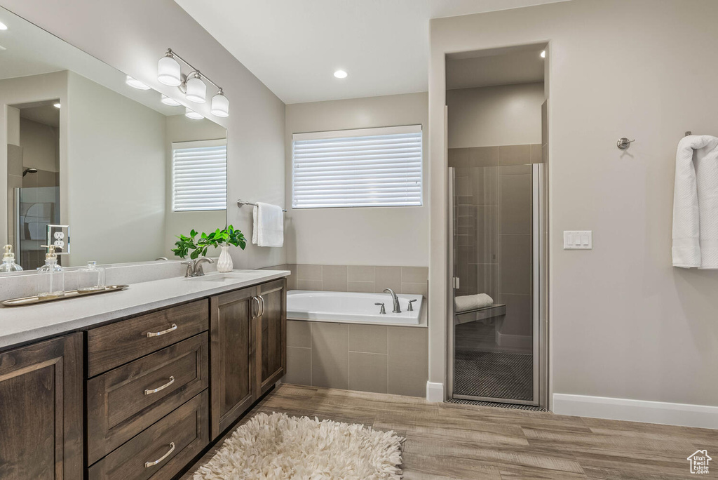 Full bathroom featuring wood finished floors, a stall shower, a bath, and vanity