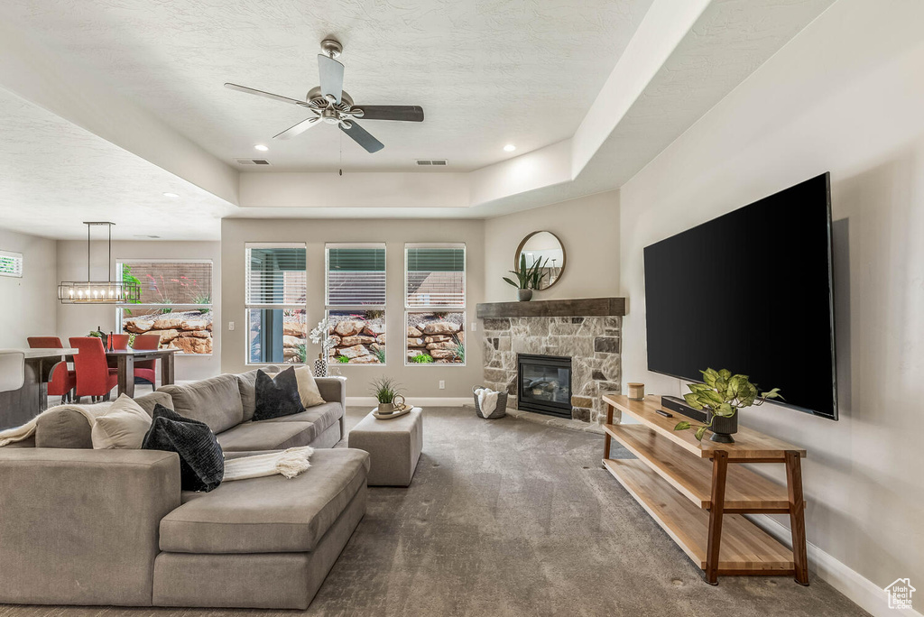 Carpeted living room featuring baseboards, a ceiling fan, a stone fireplace, a tray ceiling, and a textured ceiling