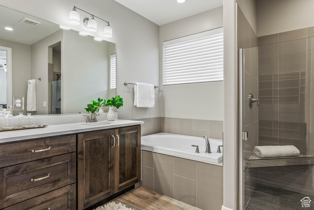 Full bathroom with a shower stall, a garden tub, vanity, wood finished floors, and recessed lighting