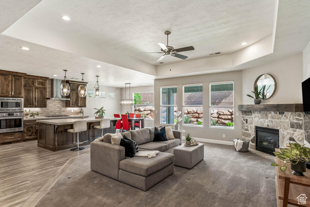 Living room with a tray ceiling, ceiling fan, a textured ceiling, baseboards, and a fireplace