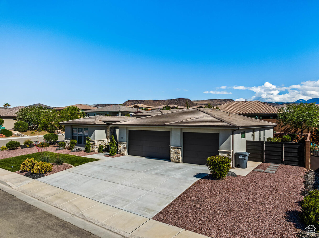 Prairie-style house featuring a garage, concrete driveway, stucco siding, fence, and stone siding