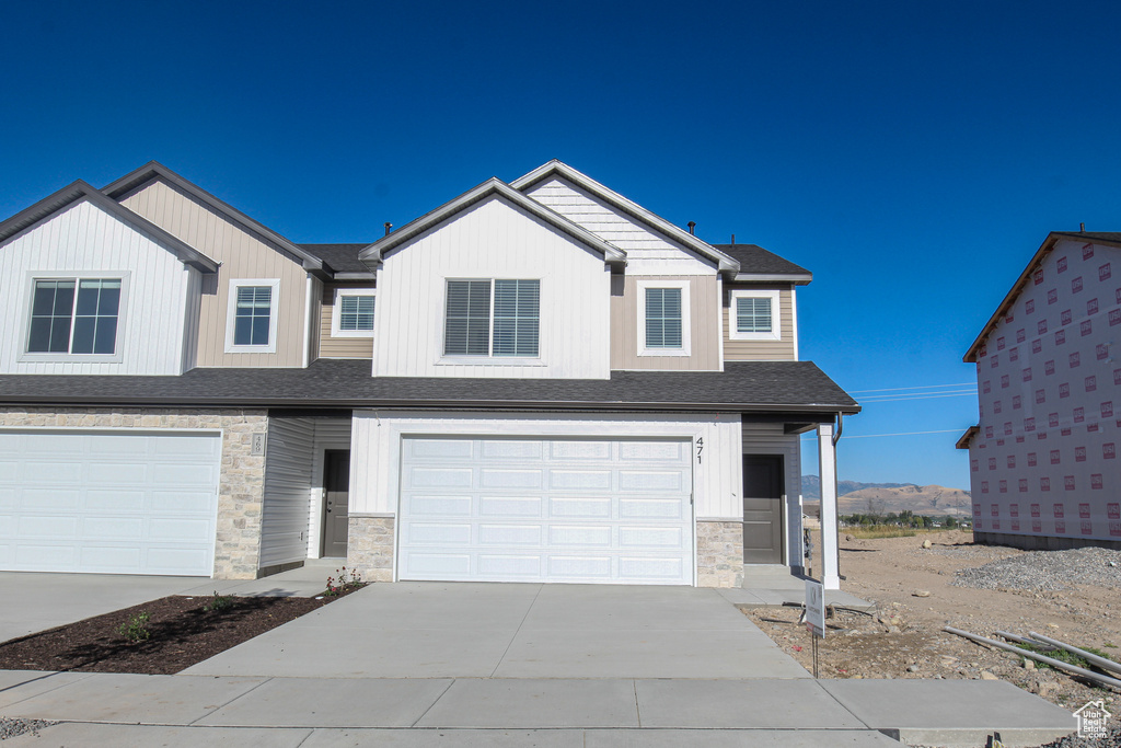 View of front facade featuring stone siding, driveway, a garage, and a shingled roof