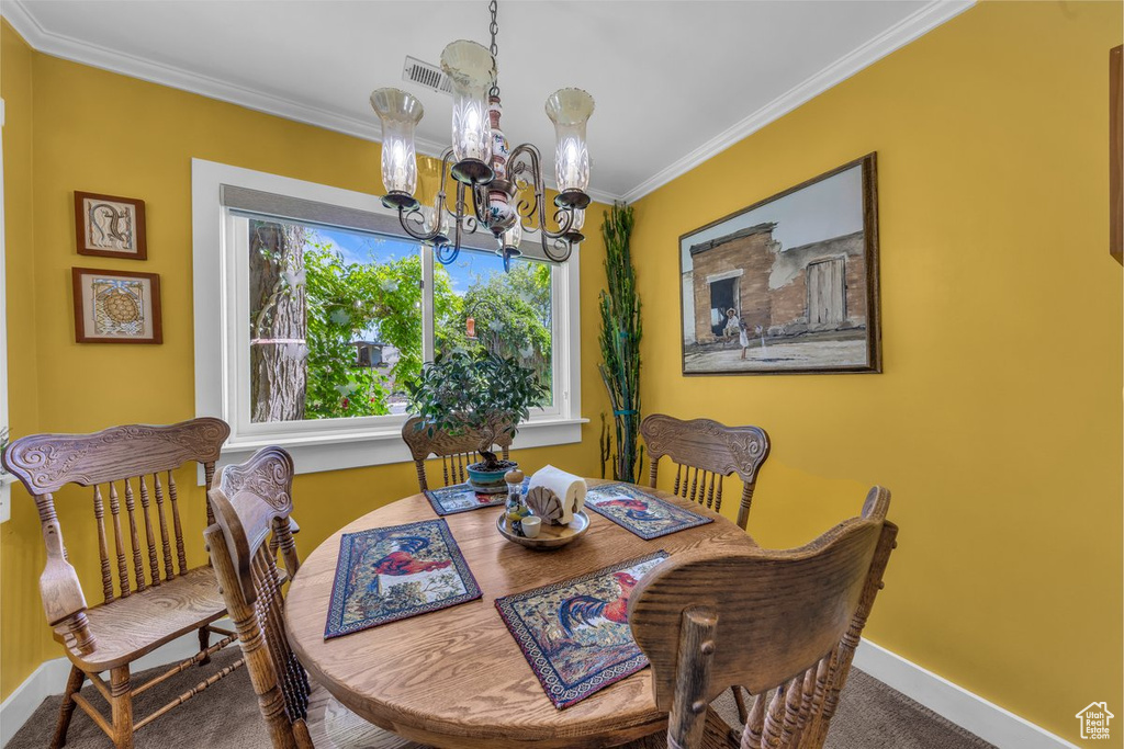 Carpeted dining area with a chandelier, ornamental molding, and baseboards