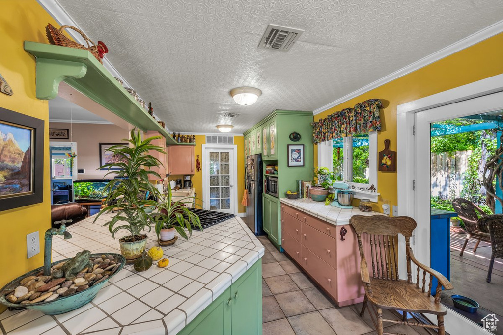 Kitchen with tile countertops, green cabinets, freestanding refrigerator, gas cooktop, and light tile patterned floors