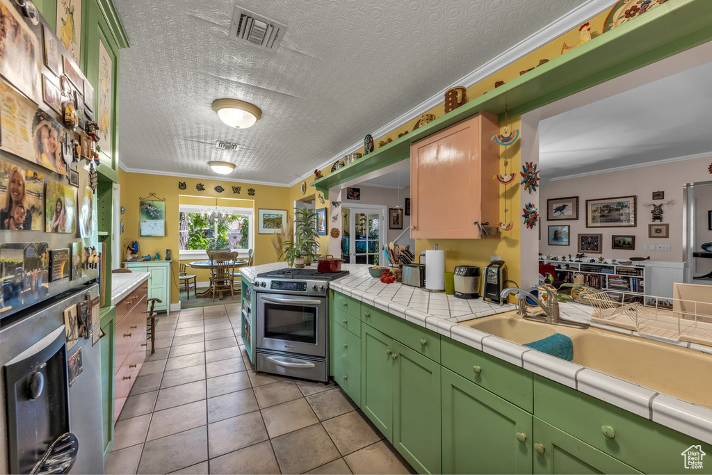 Kitchen featuring stainless steel gas range oven, fridge with ice dispenser, light tile patterned flooring, ornamental molding, and a peninsula