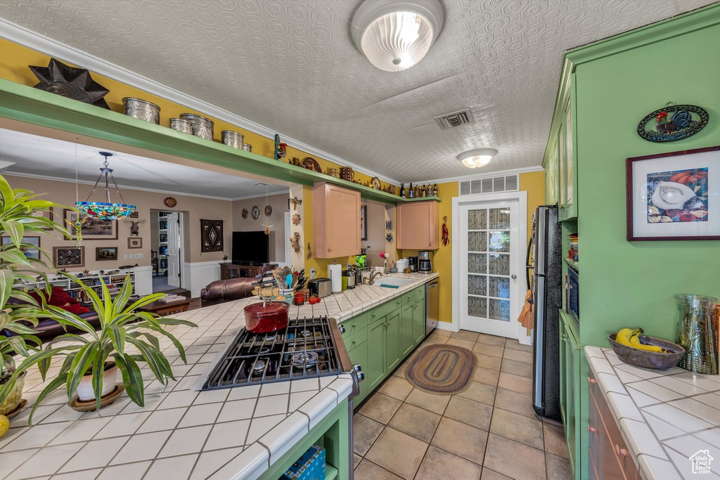 Kitchen featuring tile countertops, stainless steel appliances, a sink, crown molding, and light tile patterned flooring
